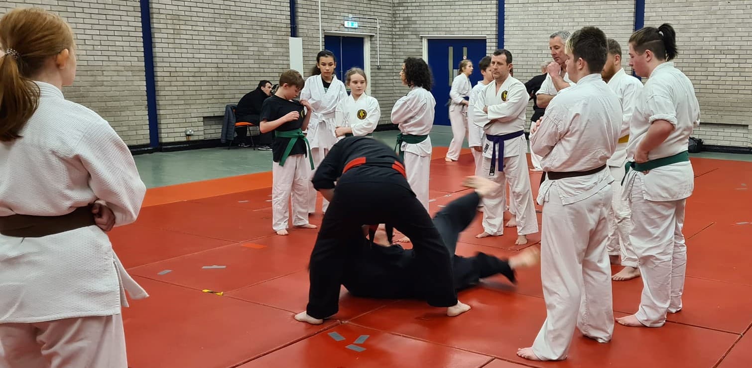 Group of martial arts students from all ages stood together watching the instructor